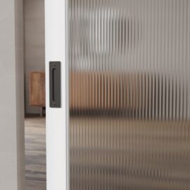 A Celine Oval Ribbed Glass Barn Door with a black handle is partially open, offering a hazy glimpse of a wooden cabinet in the background and adding an elegant touch to the barn door aesthetic.