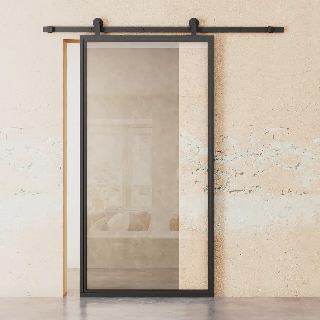 A French Casement 1-Panel Barn Door with a black metal frame is mounted on a beige textured wall, revealing a glimpse of a cozy, minimally furnished room in the background.
