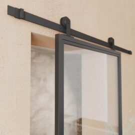 The French Casement 1-Panel Barn Door features a sliding glass panel with a black metal frame and a wall-mounted track system, perfect for indoor settings.