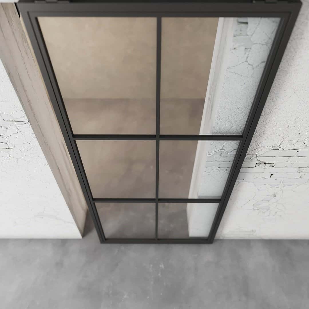 A 6-panel French Casement Barn Door with a grid pattern rests against a white, peeling wall on a concrete floor.