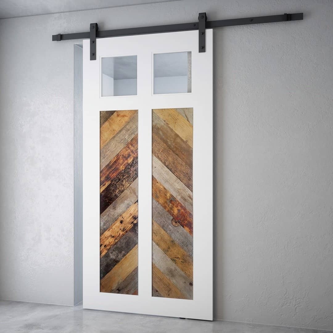 The Lake House Barn Door is a white sliding barn door featuring two rectangular windows at the top and vertical wooden panels of varying shades and textures in the middle, mounted on a black metal track.