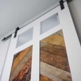 Close-up view of the Lake House Barn Door, featuring a blend of glass panes and reclaimed wood panels with a white wooden sliding design.