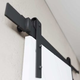 Close-up of the Prestige Barn Door hardware in black, featuring a white door mounted on a beige wall.