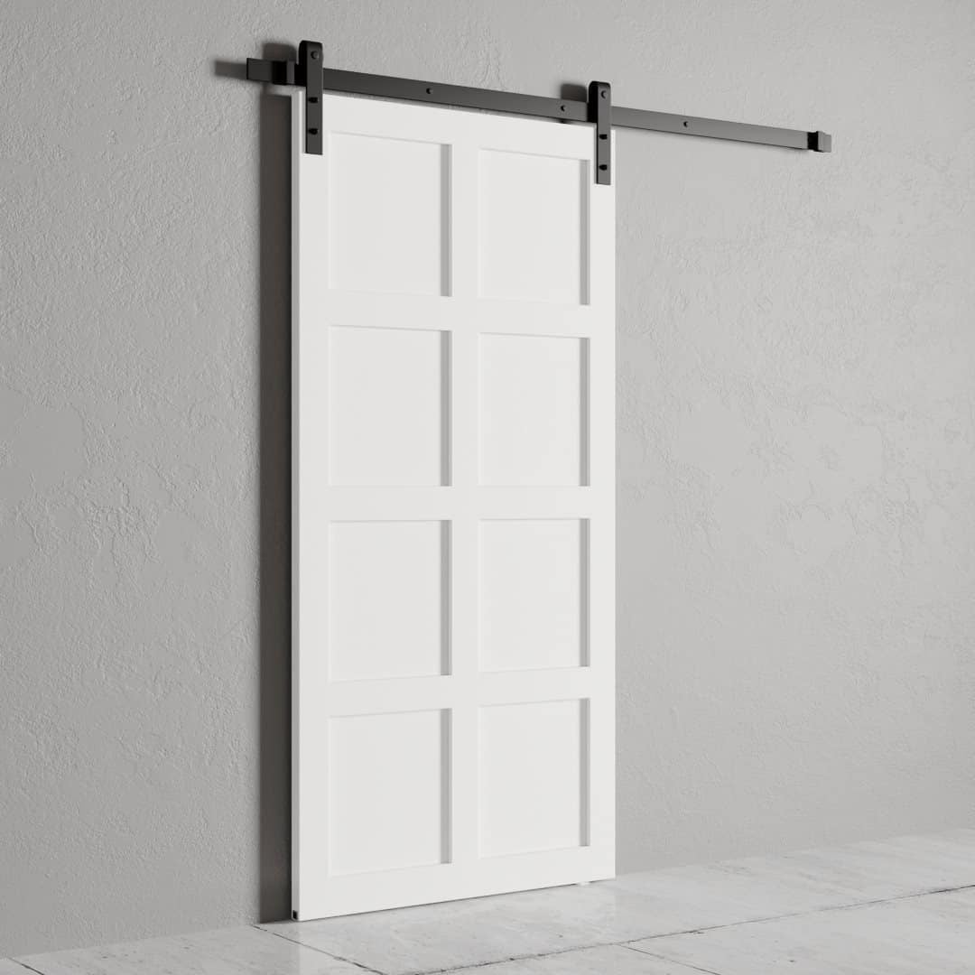 Urban-Woodcraft-8-Panel-Barn-Door-White-4.jpg An 8-Panel Barn Door with a rectangular panel design is mounted on a black sliding rail, set against a gray wall.
