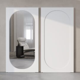 A modern interior features two large, vertical rectangular frames on a wall, one with the Celine Oval Mirror Barn Door reflecting a lounge chair and side table, and the other with a plain, decorative design.