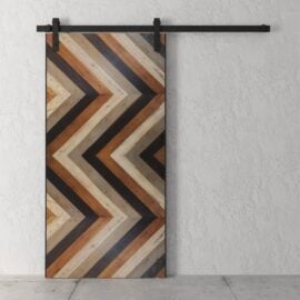 Cali Chevron Barn Door featuring a chevron wood pattern in various shades of brown and black, mounted on a black rail against a white textured wall.