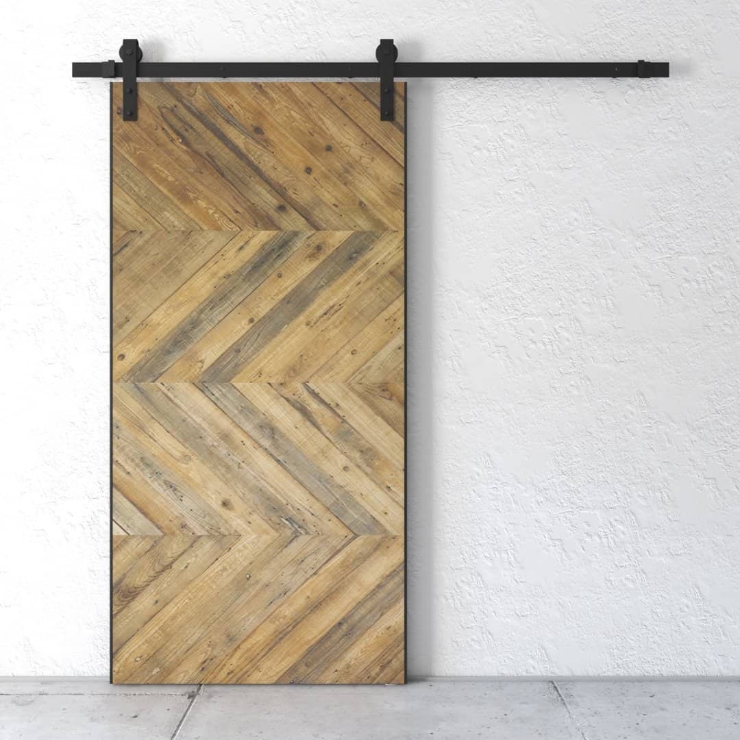 Urban-Woodcraft-Chevron-Barn-Door-Natural-1.jpg Natural Chevron Barn Door mounted on a black metal track against a textured white wall.
