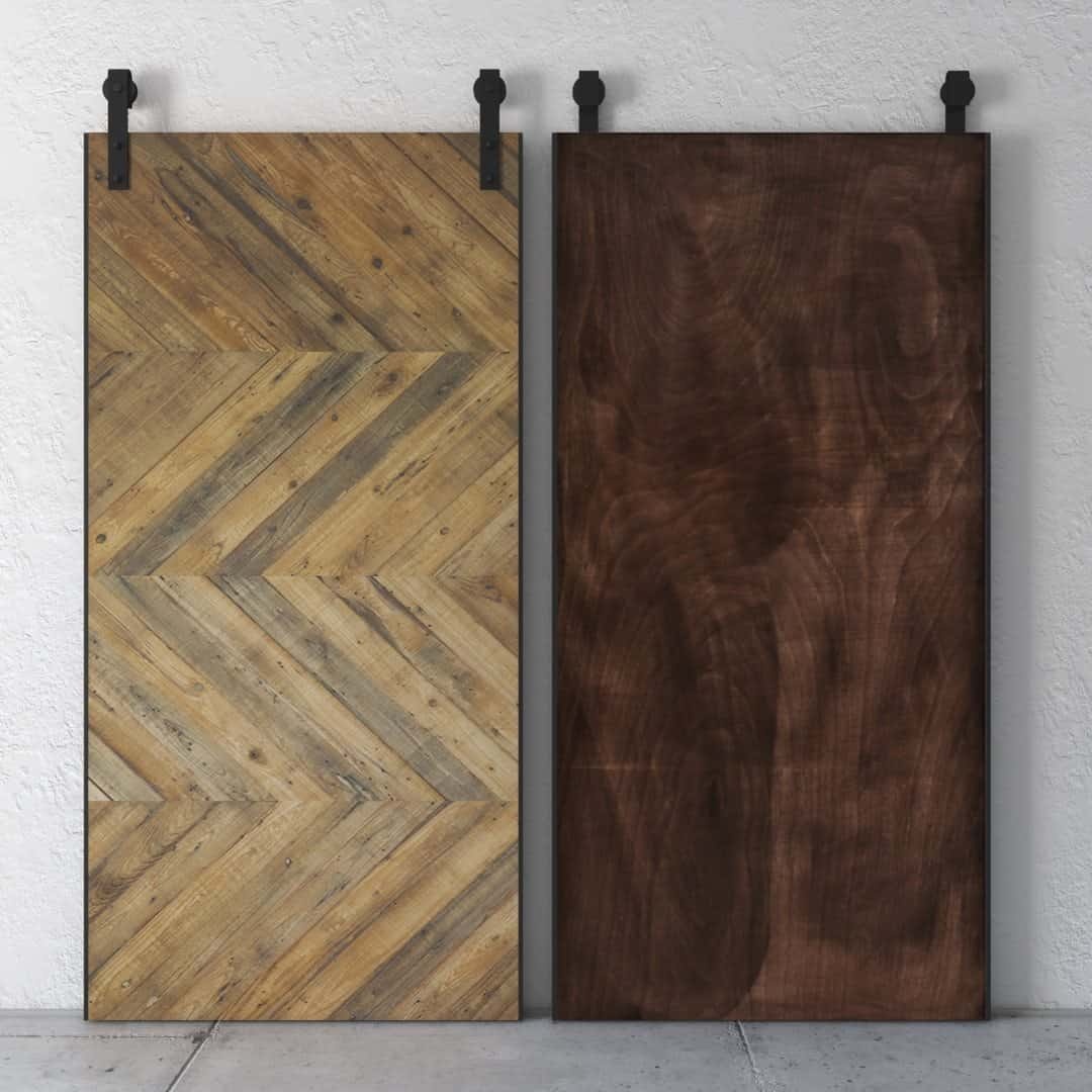 Two wooden sliding doors hang side by side on a wall. The left door, named the Natural Chevron Barn Door, features a herringbone pattern, and the right door has a smooth, dark wood finish.