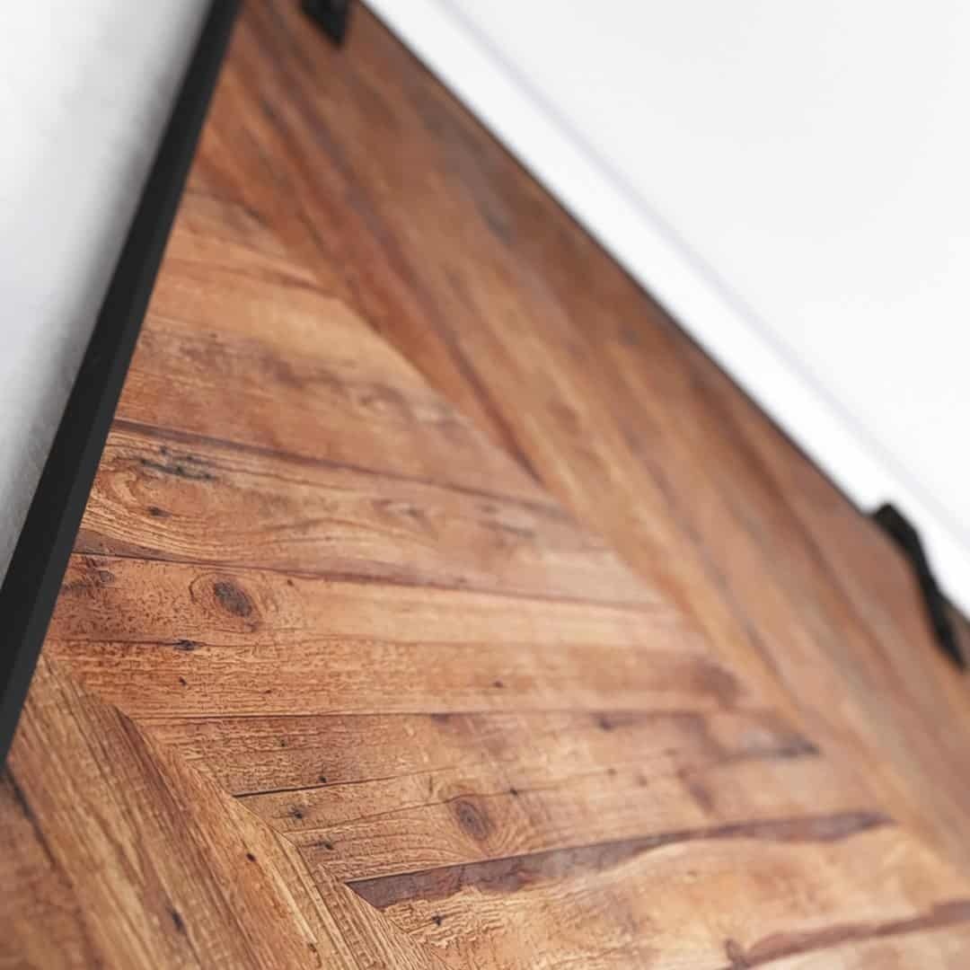 Urban-Woodcraft-Chevron-Barn-Door-Natural-3.jpg Close-up shot of the Natural Chevron Barn Door with its wooden textured surface featuring diagonal patterns, framed by dark metal edges.