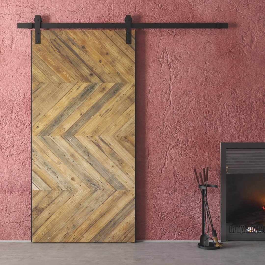 The Natural Chevron Barn Door stands next to a fireplace in a room with a textured red wall.