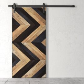 The Northwest Chevron Barn Door, featuring a chevron pattern with alternating light and dark wooden planks, is set against a white wall.