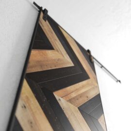 Northwest Chevron Barn Door, a wall-mounted wooden art piece, features a diagonal chevron pattern in black and natural wood tones, photographed from a low angle.