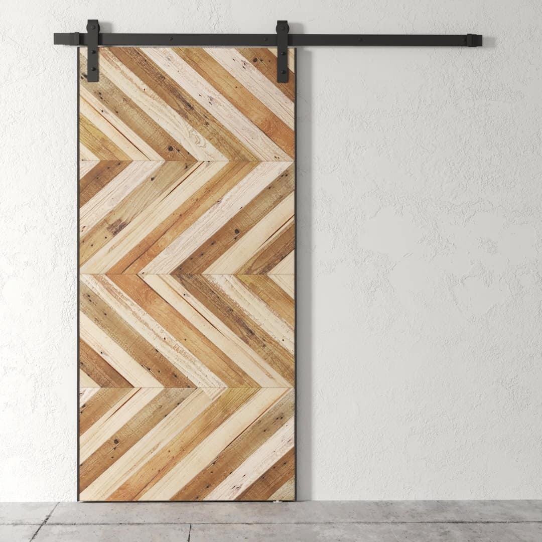 An Oasis Chevron Barn Door featuring a herringbone wood pattern is installed against a plain white wall.