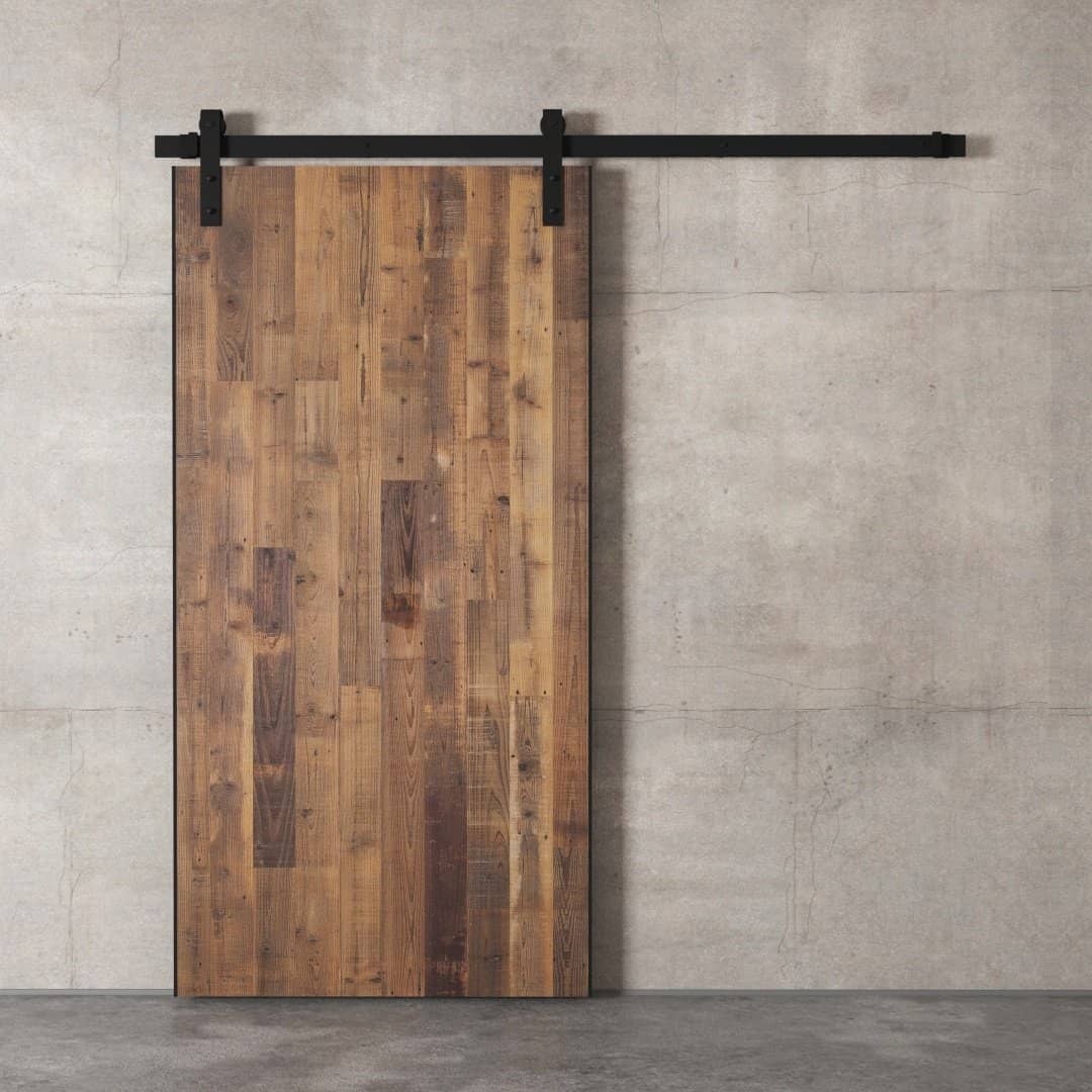 The Hampton Barn Door, featuring a wooden sliding design and a black metal track, is mounted on a plain concrete wall.