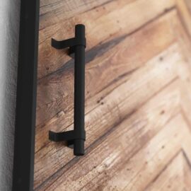 Close-up of a black metal handle on the Natural Herringbone Barn Door with a rustic finish.