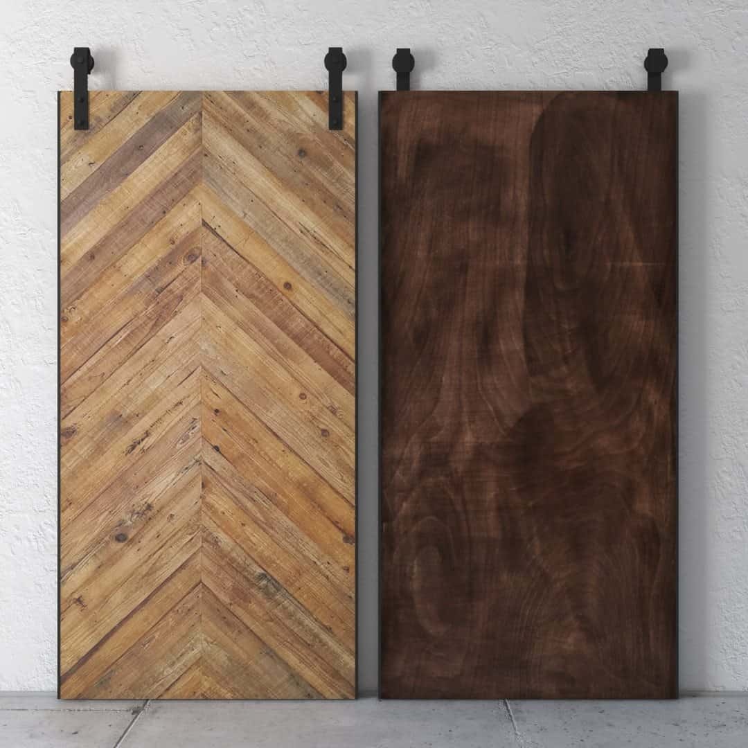 The Natural Herringbone Barn Door set features two wooden sliding doors suspended from sleek black metal tracks. The left door boasts a stylish chevron pattern, while the right door presents a smooth, dark wood finish, all perfectly contrasted against a textured white wall.