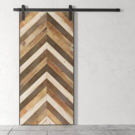 A Wolves Herringbone Barn Door made of chevron-patterned reclaimed wood with a metal rail system, set against a white textured wall.