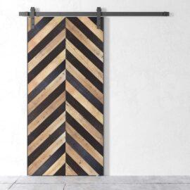 The Alchemist Herringbone Barn Door, designed with alternating light and dark planks in a herringbone pattern, stands out against a plain white wall.