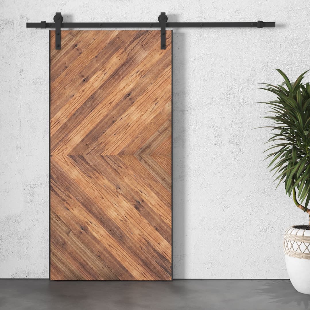 A Lucas Reclaimed Wood Arrow Barn Door on a white wall with a potted plant to the right.