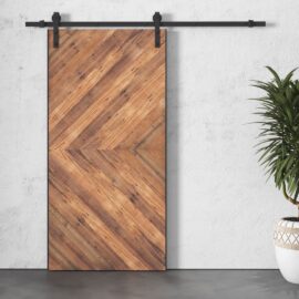 A Lucas Reclaimed Wood Arrow Barn Door on a white wall with a potted plant to the right.