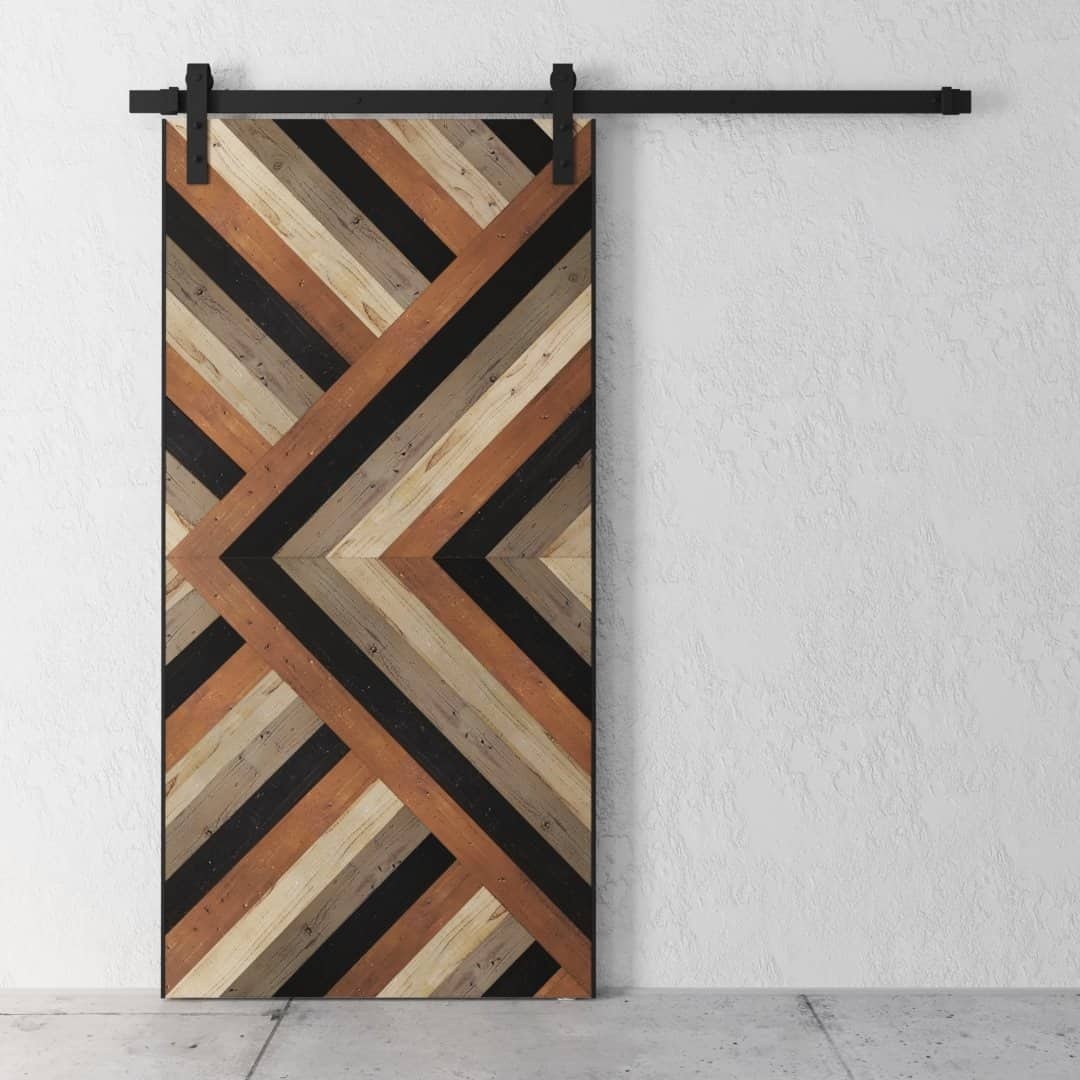 The Cali Malibu Barn Door features a geometric chevron pattern in natural, dark brown, and black finishes, mounted on a black metal track against a white textured wall.