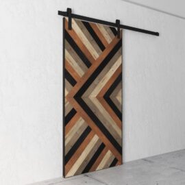 A Cali Malibu Barn Door featuring a geometric chevron pattern crafted from diverse wood tones is mounted on a black metal track in a minimalist white interior.