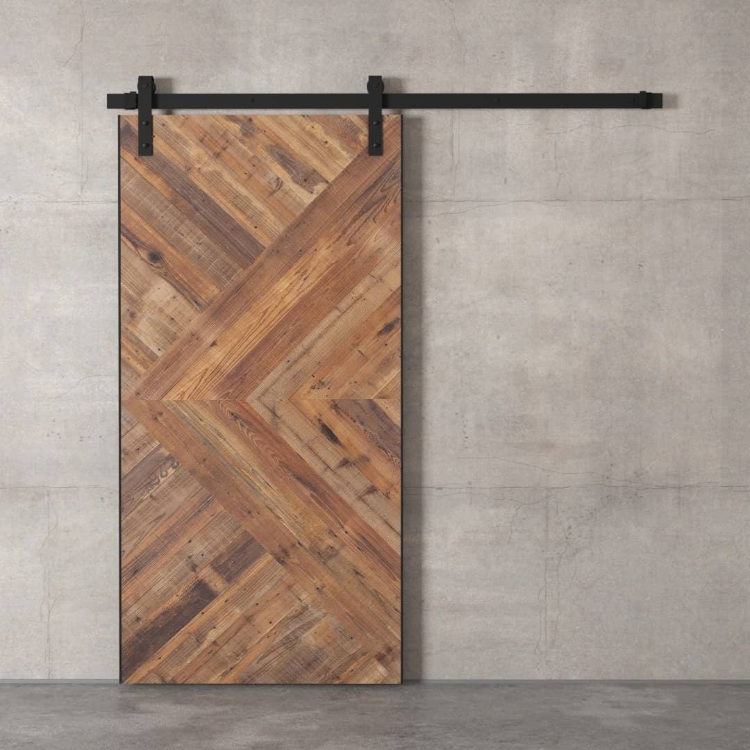 Urban-Woodcraft-Malibu-Barn-Door-Natural-1.jpg The Malibu Barn Door, featuring a wooden design with a chevron pattern, is mounted on a sleek black sliding track against a concrete wall.