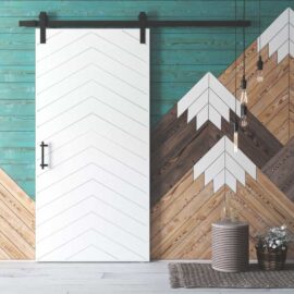The Osaka Barn Door, featuring a chevron design, slides on a black rail against a teal and wood patterned accent wall, complemented by hanging light bulbs and a small cylindrical woven stool.
