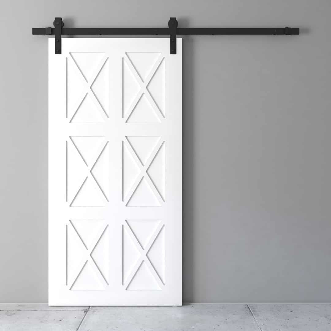 An Oxford Barn Door featuring a white, cross-pattern design is installed on a gray wall with black metal hardware.